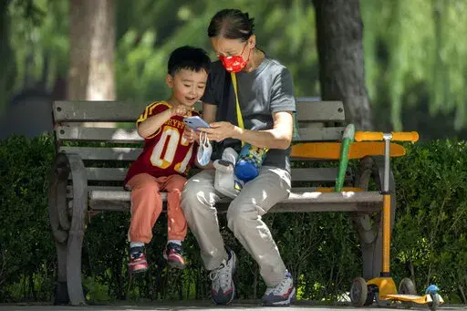 A woman wearing a face mask and a child look at a cellphone as they sit on a bench at a public park in Beijing, on June 2, 2022. As the week-long Lunar New Year holidays in China draw near with promises of feasts and red envelopes stuffed with cash, children have yet another thing to look forward to - one extra hour of online games each day. (AP Photo/Mark Schiefelbein, File)