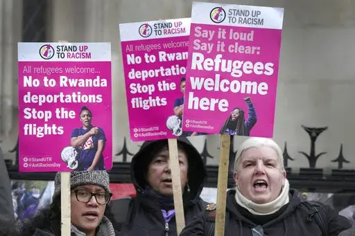 Stand Up To Racism campaigners hold banners outside the High Court in London, Monday, Dec. 19, 2022. Judges at Britain’s High Court say the U.K. government’s controversial plan to send asylum-seekers on a one-way trip to Rwanda is legal. But two judges also ruled that the government failed to consider the circumstances of the individuals it tried to deport. (AP Photo/Kirsty Wigglesworth)