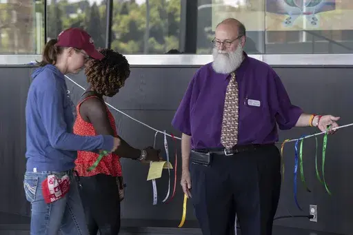 In this image provided by WSU College of Veterinary Medicine, Scott Campbell, right, Veterinary Chaplain at Washington State University's College of Veterinary Medicine, looks on as people tie ribbons honoring pets that have passed away during the Garland Ceremony, that was part of a "Celebration of Life & Remembrance for Our Companion Animals" event on Saturday, July 15, 2023, in Pullman, Wash. (Ted S. Warren/WSU College of Veterinary Medicine via AP)