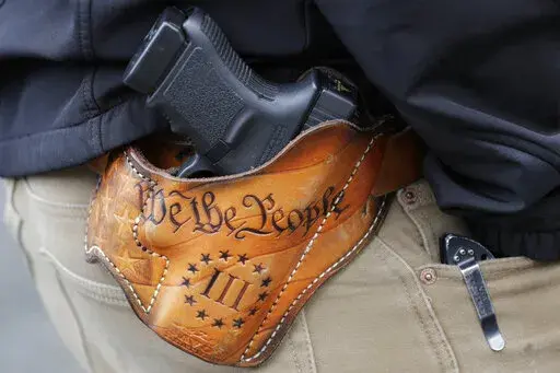 An attendee at a gun rights rally open-carries his gun in a holster that reads "We the People," from the Preamble to the United States Constitution on Jan. 18, 2019, at the Capitol in Olympia, Wash. Advocates say permitless carry makes people safer. Opponents say it makes it more dangerous for ordinary people, and for police officers. (AP Photo/Ted S. Warren, File)
