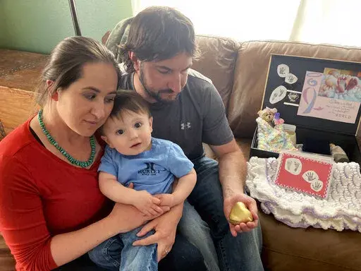 Riata Little Walker and her husband, Ian Walker, holding a heart-shaped container with their aborted daughter's ashes, are seen with their toddler son Tuesday, May 24, 2022, at their home in Casper, Wyo. Riata Little Walker is a supporter of a planned new women's health clinic in Casper that would provide abortions. It would be the only clinic of its kind in the state. (AP Photo/Mead Gruver)