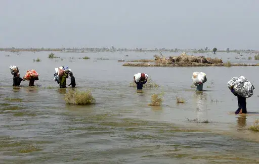 Victims of heavy flooding from monsoon rains crowd carry relief aid through flood water in the Qambar Shahdadkot district of Sindh Province, Pakistan, Sept. 9, 2022. The United Nations says weather disasters costing $200 million a day and irreversible climate catastrophe looming show the world is “heading in the wrong direction.” (AP Photo/Fareed Khan, File)