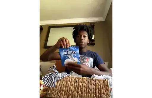 CORRECTS FIRST NAME TO CORION INSTEAD OF ORION - During a Zoom call, Friday, July 8, 2022, Corion Evans poses with candy gifted to him from the motorists he saved after their car drove off the Interstate 10 boat launch and into the Pascagoula River, in Mississippi, early Sunday, July 3. (AP Photo/Carrie Antlfinger)