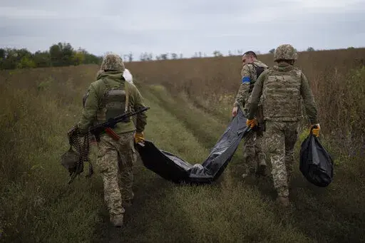 Ukrainian servicemen carry a bag containing the body of a Ukrainian soldier, center, as one of them, right, carries the remains of a body of a Russian soldier in a retaken area near the border with Russia in Kharkiv region, Ukraine, Saturday, Sept. 17, 2022. (AP Photo/Leo Correa)