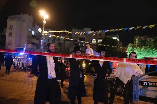 Ultra-Orthodox Jews stand behind police tape after a stabbing attack in the town of Elad, Israel, Thursday, May 5, 2022. Israeli medics say at least three people were killed in a stabbing attack near Tel Aviv on Thursday night. Israeli police said they suspect it was a militant attack. (AP Photo/Maya Alleruzzo)