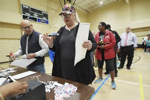 Blythe Gonzalez, right, asks a question of a Jackson, Miss., precinct worker, unseen, while her husband Jorge Gonzalez, left, waits with his paper ballot, to accompany her to a voting kiosk, Nov. 5, 2024. (AP Rogelio V. Solis, File)