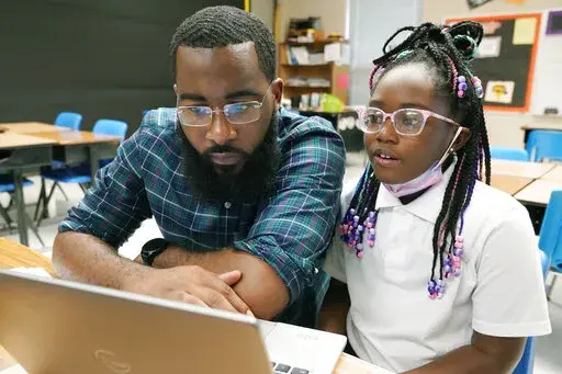 Ryan Johnson, a fifth-grade teacher at Pecan Park Elementary School, left, checks to see what homework his daughter, Rylei, is bringing home, as they prepare to leave Johnson's classroom in Jackson, Miss., Tuesday, Sept. 6, 2022. Because the city's long-standing water issues recently forced the public schools to again revert to remote learning, Johnson brought his daughter to work where she could be monitored as she also attended virtual classes, while he taught his students virtually. (AP Photo