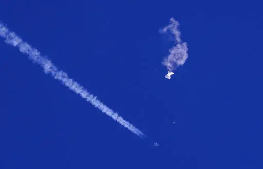 In this photo provided by Chad Fish, the remnants of a large balloon drift above the Atlantic Ocean, just off the coast of South Carolina, with a fighter jet and its contrail seen below it, Saturday, Feb. 4, 2023. The downing of the suspected Chinese spy balloon by a missile from an F-22 fighter jet created a spectacle over one of the state's tourism hubs and drew crowds reacting with a mixture of bewildered gazing, distress and cheering. (Chad Fish via AP)