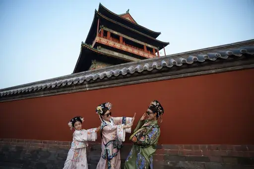 Chinese girls dressed in Qing Dynasty attire take pictures outside the Drum Tower at Gulou East Street in Beijing, China, Tuesday, July 16, 2024. (AP Photo/Vincent Thian)