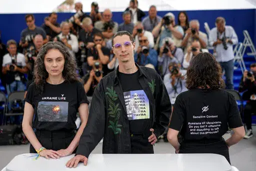 Producers Darya Bassel, left, and Yelizaveta Smith, right, wearing t-shirts that have an image of an explosion on the front and read "Sensitive Content: Russians kill Ukrainians. Do you find it offensive and disturbing to talk about this genocide?" pose with director Maksym Nakonechnyi who wears a t-shirt that reads "Free Tayra" in reference to Julia Paevska, aka Tayra, a Ukrainian medic who Russian forces have taken captive at the photo call for the film 'Butterfly Vision' at the 75th internati