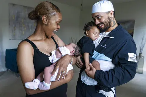 Aaliyah Wright, 25, of Washington, reacts on seeing a smile from her newborn daughter Kali, as her husband Kainan Wright, 24, of Washington, holds their son Khaza, 1, during a visit to the children's grandmother in Accokeek, Md., Tuesday, Aug. 9, 2022. A landmark social program is being pioneered in the nation’s capital. Coined “Baby Bonds,” the program is designed to narrow the wealth gap. The program would provide children of the city’s poorest families up to $25,000 when they reach ad