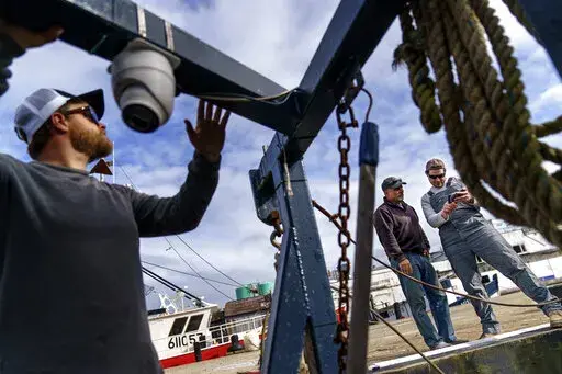 Mark Hager, left, positions a camera with the help of Anthony Lucia, right, as captain Al Cottone watches the feed on a monitor from his boat, the Sabrina Maria, in Gloucester, Mass., May 11, 2022. Hager's Maine-based startup, New England Maritime Monitoring, is one of a bevy of companies seeking to help commercial vessels comply with new federal mandates aimed at protecting dwindling fish stocks. But taking the technology overseas, where the vast majority of seafood consumed in the U.S. is caug
