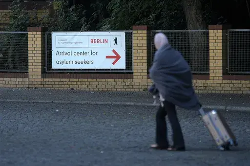 A woman with a trolley leaves the central registration center for asylum seekers in Berlin, Germany, Tuesday, Sept. 26, 2023. Across Germany, officials are sounding the alarm that they are no longer in a position to accommodate migrants who are applying for asylum. (AP Photo/Markus Schreiber)