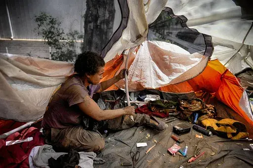 Suffering from homelessness Esca Guernon fixes her tent that's set up at an encampment next to the 405 Freeway in the Van Nuys section of Los Angeles on Friday, July 26, 2024, in Los Angeles. California Gov. Gavin Newsom has issued an executive order directing state agencies "to move urgently to address dangerous" homeless encampments and clear them from state land while giving city and local leaders a push to do the same. (AP Photo/Jae C. Hong)
