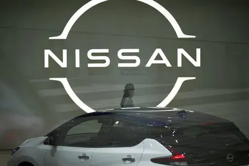 A staff walking near a Nissan logo at Nissan headquarters is seen though a window on May 12, 2022, in Yokohama near Tokyo. Nissan and Renault have changed their mutual cross-shareholdings to the same 15%, ironing out a source of conflict in the Japan-French auto alliance. (AP Photo/Eugene Hoshiko, File)