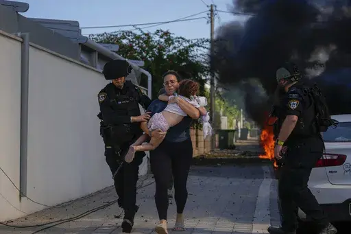 Israeli police officers evacuate a woman and a child from a site hit by a rocket fired from the Gaza Strip, in Ashkelon, southern Israel, Saturday, Oct. 7, 2023. Thousands of Hamas-led militants storm across the border into Israel, killing 1,200 people, mostly civilians, and taking roughly 250 captive, according to Israeli authorities. (AP Photo/Tsafrir Abayov, File)