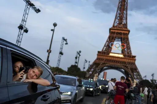 Passengers in the back of a taxi film themselves as they leave the Eiffel Tower decorated with the Olympic rings ahead of the 2024 Summer Olympics, Wednesday, July 17, 2024, in Paris. The city itself will be one of the protagonists of the 2024 Olympics. That's why the Eiffel Tower and Seine River are featured just as prominently as Simone Biles or Katie Ledecky in NBC’s ads. (AP Photo/David Goldman, File)