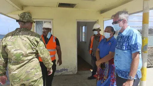 In this photo released by the New Zealand High Commission, Peter Lund, right, New Zealand’s acting high commissioner to Tonga, stands with military personnel at a wharf in Nuku'alofa, Tonga Friday, Jan. 21, 2022, after a New Zealand ship arrived with water and other much-needed aid supplies. (New Zealand High Commission via AP)
