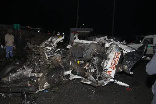 CORRECTS DATE - People stand near the wreckage of vehicles after a fatal accident in Londiani, Kenya, Friday, June 30, 2023, at a location known for crashes about 200 kilometers (125 miles) northwest of the capital, Nairobi. Dozens were killed when a truck rammed into several other vehicles and market traders on Friday evening, police said. (AP Photo)