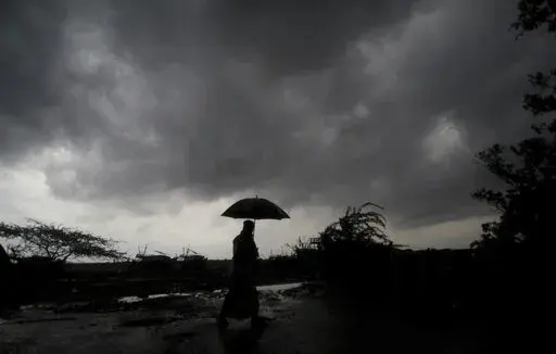 A villager holds an umbrella as dark clouds loom over Balasore district in Odisha, India, Tuesday, May 25, 2021, ahead of a powerful storm barreling toward the eastern coast. When it comes to measuring global warming, it’s not just the heat, it’s the humidity that matters in dangerous climate extremes, according to a study released on Monday, Jan. 31, 2022, in the Proceedings of the National Academy of Sciences in the U.S. (AP Photo/File)