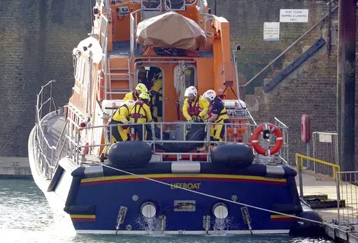 Members of the Dover lifeboat place a body bag on a stretcher after returning to the Port of Dover after a large search and rescue operation launched in the Channel off the coast of Dungeness, in Kent, Wednesday Dec. 14, 2022, following an incident involving a small boat likely to have been carrying migrants. Helicopters and lifeboats have been dispatched to the English Channel off the coast of Kent in southern England to rescue a small boat in distress, authorities said Wednesday. (Gareth Fulle