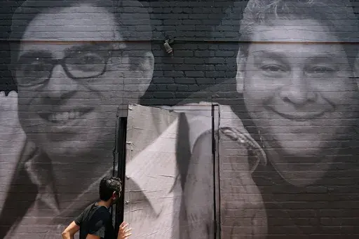A woman steps through a door that is covered by a mural depicting American hostages and wrongful detainees who are being held abroad, July 20, 2022, in the Georgetown neighborhood of Washington. At left is Siamak Namazi, who has been in captivity in Iran since 2015. At right is Jose Angel Pereira, who has been imprisoned in Venezuela since 2017. The Biden administration has cleared the way for the release of five American citizens detained in Iran, including Namazi, by issuing a blanket waiver f