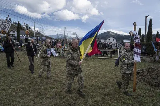 Ukrainian servicemen carry national flags and photos of their comrade Vasyl Boichuk who was killed in Mykolayiv in March 2022, during his funeral ceremony at the cemetery in Iltsi village, Ukraine, Tuesday, Dec. 26, 2023. (AP Photo/Evgeniy Maloletka)