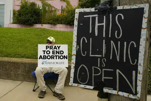An anti-abortion supporter sits behind a sign that advises the Jackson Women's Health Organization clinic is still open in Jackson, Miss., Wednesday, July 6, 2022. (AP Photo/Rogelio V. Solis, File)