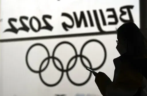 A woman looks at her phone as she passes an Olympic logo inside the main media center for the 2022 Winter Olympics, Jan. 18, 2022, in Beijing. (AP Photo/David J. Phillip, File)