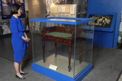 Luci Baines Johnson looks at the desk on May 16, 2023, on display at the LBJ Presidential Library, that President Lyndon B. Johnson sat at in the President's Room at the U.S. Capitol to sign the Voting Rights Act of 1965, on Aug. 6, 1965. Concern for U.S. democracy amid deep national polarization has prompted the entities supporting 13 presidential libraries dating back to Herbert Hoover to call for a recommitment to the country's bedrock principles, including the rule of law and respecting a di