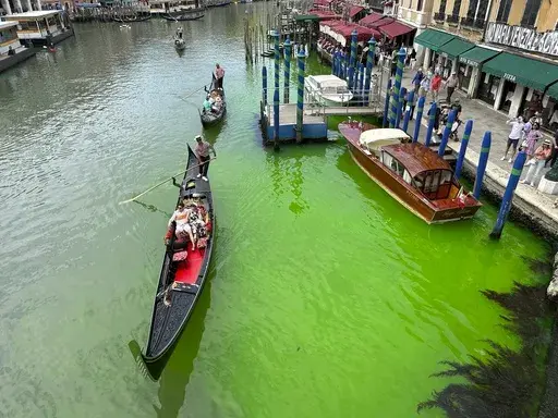 A bright patch of green is seen in the Grand Canal along an embankment lined with restaurants, in Venice, Italy, Sunday, May 28, 2023. Police in Venice are investigating the source of a phosphorescent green liquid patch that appeared Sunday in the city's famed Grand Canal. (AP Photo/Luigi Costantini)
