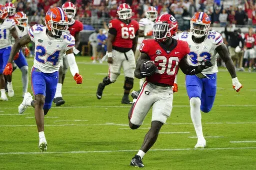 Georgia running back Daijun Edwards (30) runs for a 22-yard touchdown past Florida cornerback Avery Helm (24) and defensive lineman Princely Umanmielen (33) during the second half of an NCAA college football game Saturday, Oct. 29, 2022, in Jacksonville, Fla. (AP Photo/John Raoux)