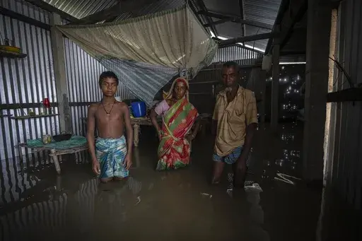 Yaad Ali, right, and his wife Monuwara Begum, center, and Musikur Alam, stand in their submerged house in Sandahkhaiti, a floating island village in the Brahmaputra River in Morigaon district, Assam, India, Wednesday, Aug. 30, 2023. The family move away with every flood, and move back to their house every dry season. (AP Photo/Anupam Nath, File)