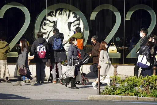 People wearing protective masks to help curb the spread of the coronavirus stand outside a window displaying a 2022 New Year celebration along a street Wednesday, Dec. 29, 2021, in Tokyo. (AP Photo/Eugene Hoshiko)