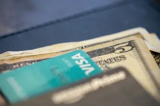 In this Aug. 11, 2019 file photo, U.S. currency and credit cards sit on a table at a restaurant in New Orleans. People who make money on the side usually declare self-employment income. They’re running businesses, even if they’re very small ones — and by treating them as such, people with side gigs may be able to optimize their time spent working to reach their personal financial goals more efficiently. (AP Photo/Jenny Kane, File)