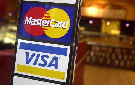 This April 22, 2005, file photo, shows logos for MasterCard and Visa credit cards at the entrance of a New York coffee shop. Visa and MasterCard announced, Tuesday, March 26, 2024, a settlement with U.S. merchants related to swipe fees, a development that could potentially save consumers tens of billions of dollars. (AP Photo/Mark Lennihan, File)