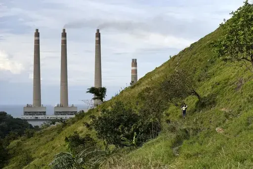 A couple walk on a hill called 'Teletubbies Hill', a locally popular tourist attraction, as the chimneys of Suralaya coal power plant looms in the background, in Cilegon, Indonesia, Sunday, Jan. 8, 2023. Asia must rapidly cut fossil fuel subsidies and plow more money into a clean energy transition to avoid catastrophic climate change that puts its own development at risk, according to a new report Thursday, April 27, from the Asian Development Bank. (AP Photo/Dita Alangkara)