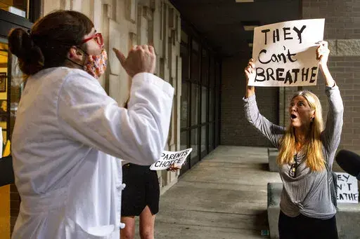 Dr. Brooke Decker, left, of Marshall, Director of Infection Prevention, argues with Dana Gibson about her opposition to a mask mandate for students before the North Allegheny School District school board regarding the district's mask policy, Aug. 25, 2021, at at North Allegheny Senior High School in McCandless, Pa. During earlier surges of the COVID-19 pandemic, some governors ordered business closures, issued mask mandates and required vaccines in certain settings. Some even required quarantine