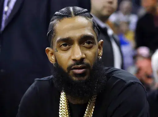 Rapper Nipsey Hussle attends an NBA basketball game between the Golden State Warriors and the Milwaukee Bucks in Oakland, Calif., March 29, 2018. Three years after rapper Hussle was gunned down outside a Los Angeles clothing store that he founded to help revitalize the neighborhood where he grew up, a trial will finally begin Wednesday, June 15, 2022, for the man charged with killing him. (AP Photo/Marcio Jose Sanchez, File)