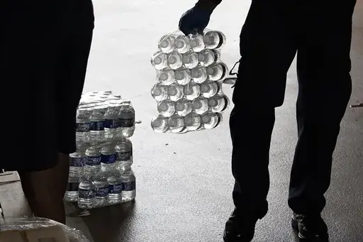 A recruit for the Jackson Fire Department carries a case of bottled water to a resident's car, Aug. 18, 2022, as part of the city's response to longstanding water system problems in Jackson, Miss. (AP Photo/Rogelio V. Solis, File)