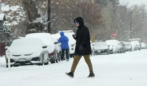 A pedestrian crosses First Avenue as a winter storm sweeps over the intermountain West, plunging temperatures into the single digits and bringing along a light snow in its wake Saturday, Jan. 18, 2025, in Denver. (AP Photo/David Zalubowski)