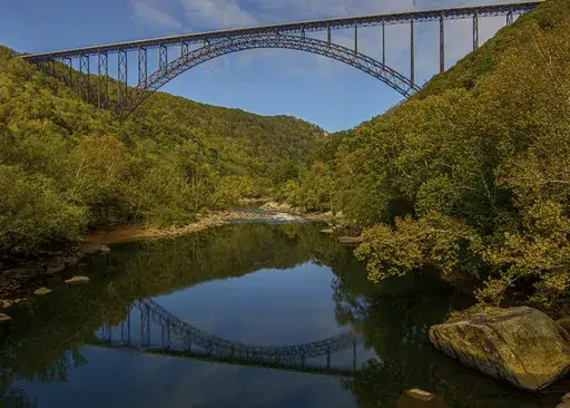 The New River Gorge Bridge is reflected in the water as seen from Fayette Station, Oct. 9, 2019, in Fayetteville, W.Va. A program offering cash and free outdoor adventures to remote workers to move to West Virginia with the hope of offsetting population losses has added the New River Gorge region where out-of-state workers can apply to live. The public-private program Ascend West Virginia said Tuesday, June 20, 2023, that applications are being accepted for the scenic region. (F. Brian Ferguson/