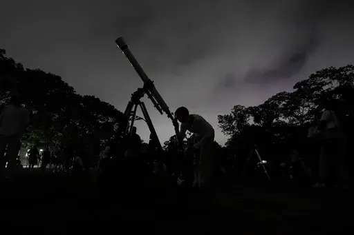 A girl looks at the moon through a telescope in Caracas, Venezuela, on Sunday, May 15, 2022. Six planets will line up in the early morning sky on June 3, 2024 but most won't be visible to the naked eye. A planetary parade happens relatively often when several planets align on the right side of the sun, making them visible across a narrow band of our sky. (AP Photo/Matias Delacroix)
