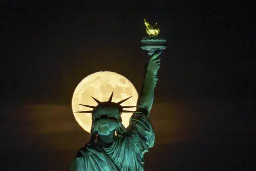The Strawberry Supermoon rises in front of the Statue of Liberty in New York, late Tuesday, June 14, 2022. (AP Photo/J. David Ake)