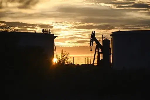 The sun begins to set behind crude oil tanks and a pumpjack, July 5, 2022, in Midland, Texas. The IEA’s annual world energy outlook, which analyzes the global picture of energy supply and demand, was released Tuesday, Oct. 24, 2023. (Eli Hartman/Odessa American via AP, File)
