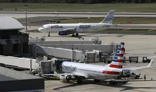 A JetBlue Airbus A320 taxis to a gate on Oct. 26, 2016, after landing, as an American Airlines jet is seen parked at its gate at Tampa International Airport in Tampa, Fla. The two airlines must abandon their partnership in the northeast United States, a federal judge in Boston ruled Friday, May 19, 2023, saying that the government proved that the deal reduces competition in the airline industry. (AP Photo/Chris O'Meara, File)
