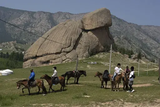 Tourists enjoy horseback riding near the iconic Turtle Rock outcrop at the Terejl National Park outside Ulaanbaatar, Mongolia on July 3, 2024. (AP Photo/Ng Han Guan)