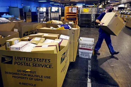A worker carries a large parcel at the United States Postal Service sorting and processing facility Nov. 18, 2021, in Boston. Congress would lift onerous budget requirements that have helped push the Postal Service deeply into debt and would require it to continue delivering mail six days per week under bipartisan legislation that approached House approval Tuesday, Feb. 8, 2022. (AP Photo/Charles Krupa, File)