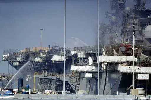 Fire crews spray water from the dock onto the side of the USS Bonhomme Richard, in San Diego, July 12, 2020. No one disputes that the Navy shares blame for the loss of the USS Bonhomme Richard, the $1.2 billion amphibious assault ship that was consumed by flames in San Diego in July 2020 as officers failed to respond quickly and its crew struggled with broken equipment. But none of that would not have happened, according to prosecution closing arguments Thursday, Sept. 29, 2022, without Ryan Saw