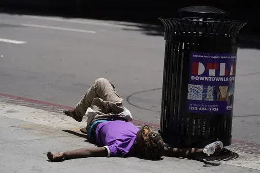A homeless person lies on the sidewalk while holding a water bottle, Sunday, July 2, 2023, in downtown Los Angeles. Excessive heat warnings remain in place in many areas across the U.S. and are expected to last at least through Monday. (AP Photo/Damian Dovarganes, File)